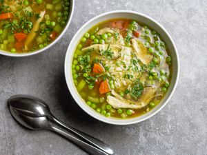 Chicken and rice soup fills two white bowls. Two spoons lay beside them.