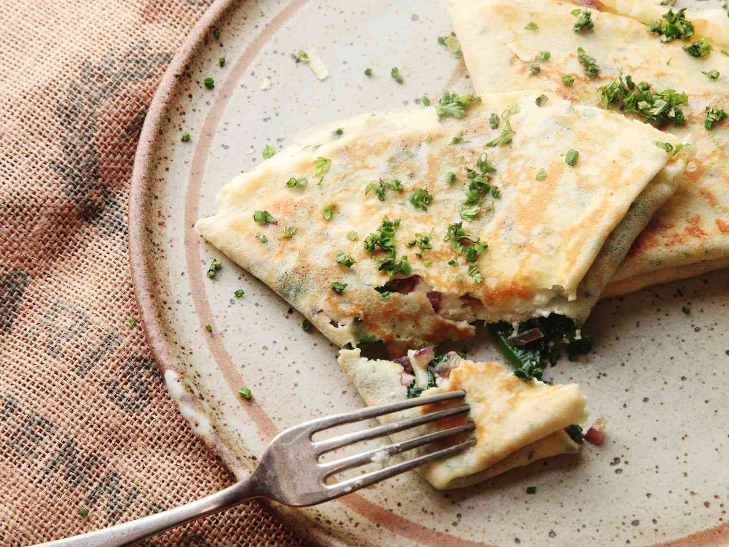 A plate of French crepes with spinach and feta, sprinkled with herbs on top. 