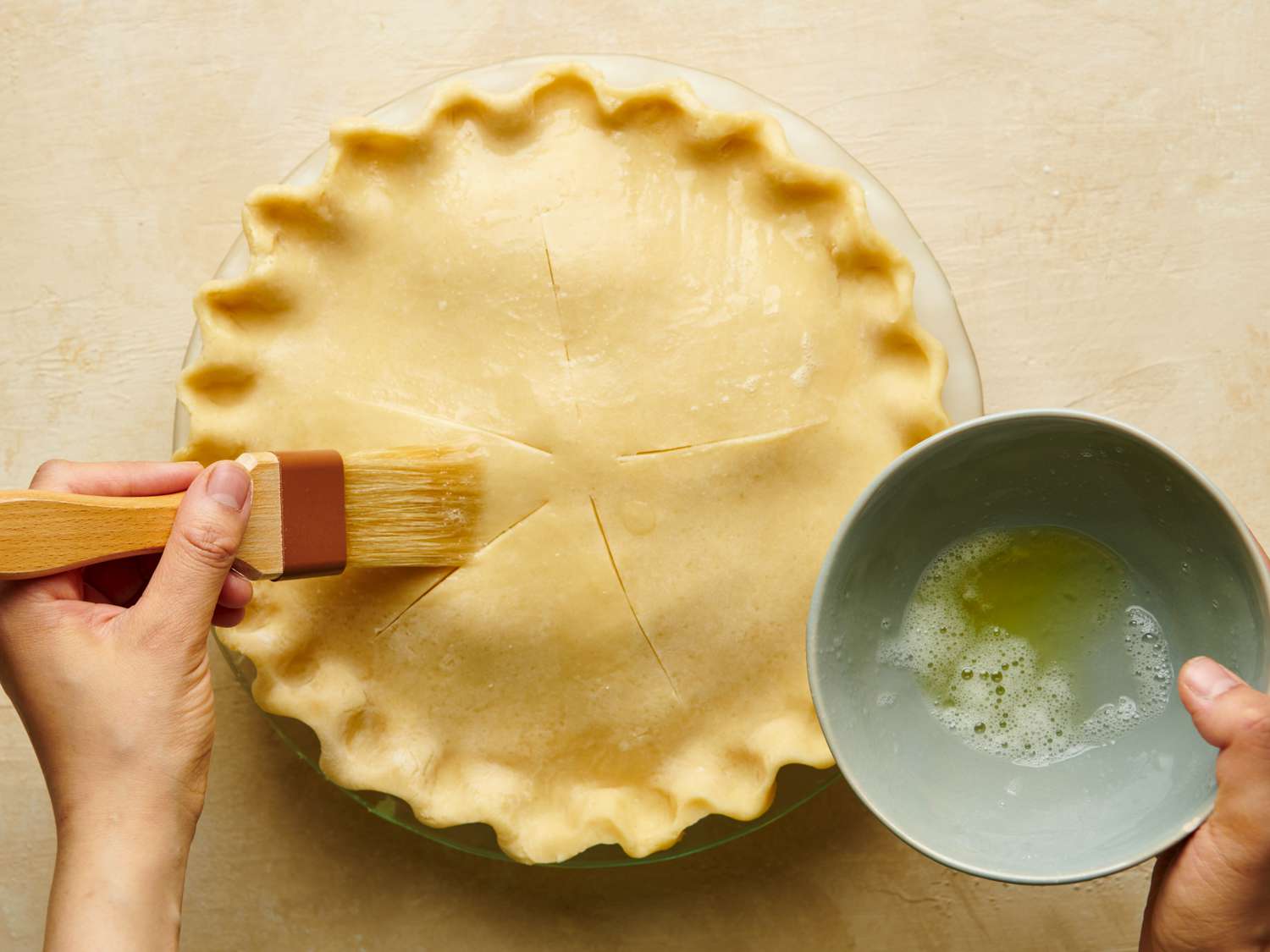 The surface of the pie being brushed with lightly beaten egg.