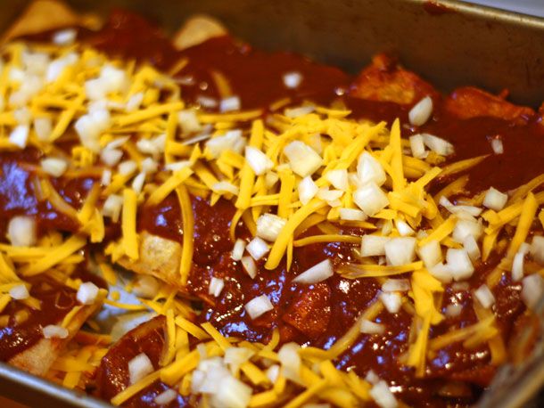 A baking pan full of Tex-Mex enchiladas smothered in red chili gravy and topped with shredded cheddar and chopped onion.