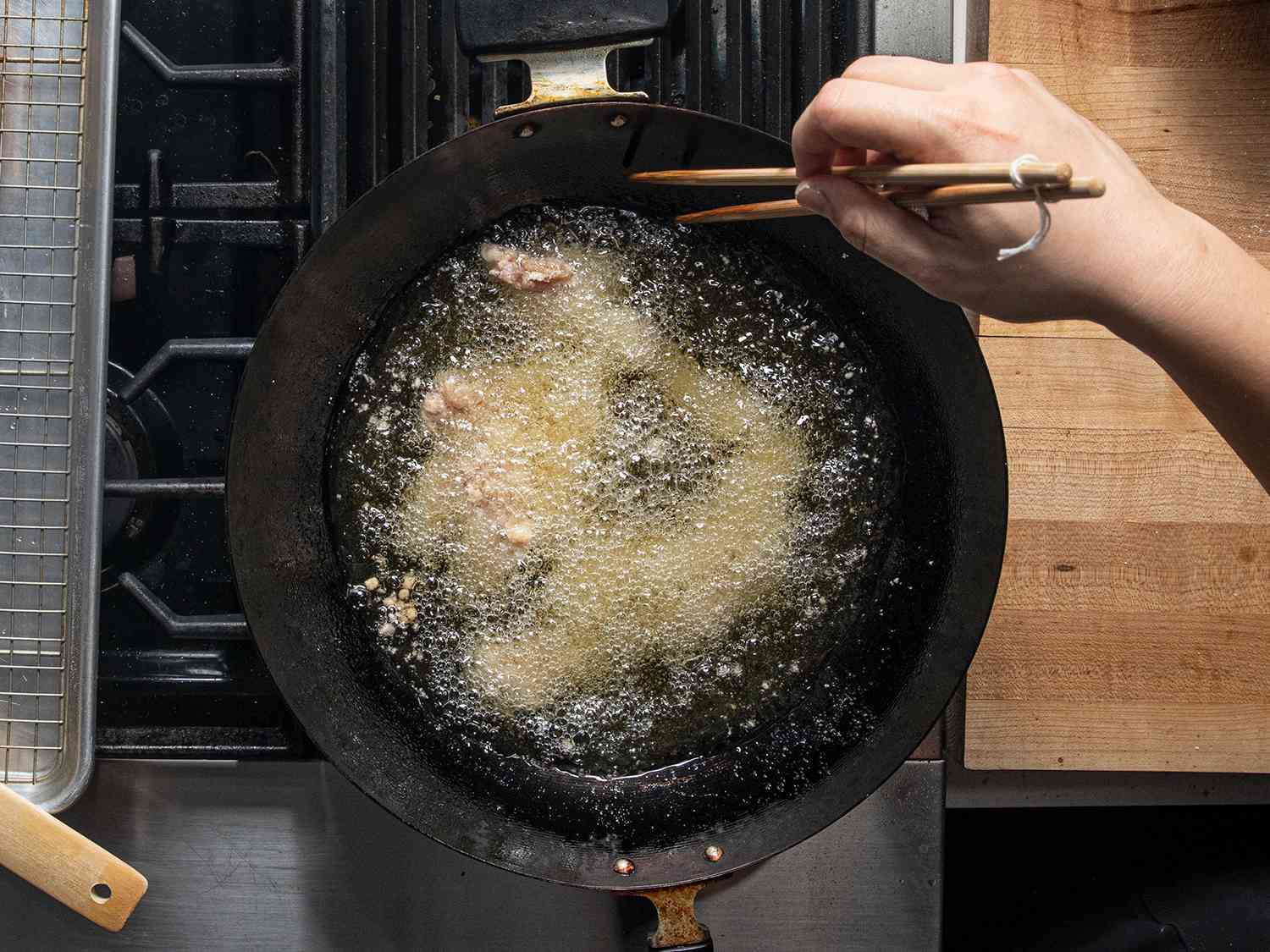 An overhead view of chicken deep-frying in a wok and being stirred with a pair of chopsticks