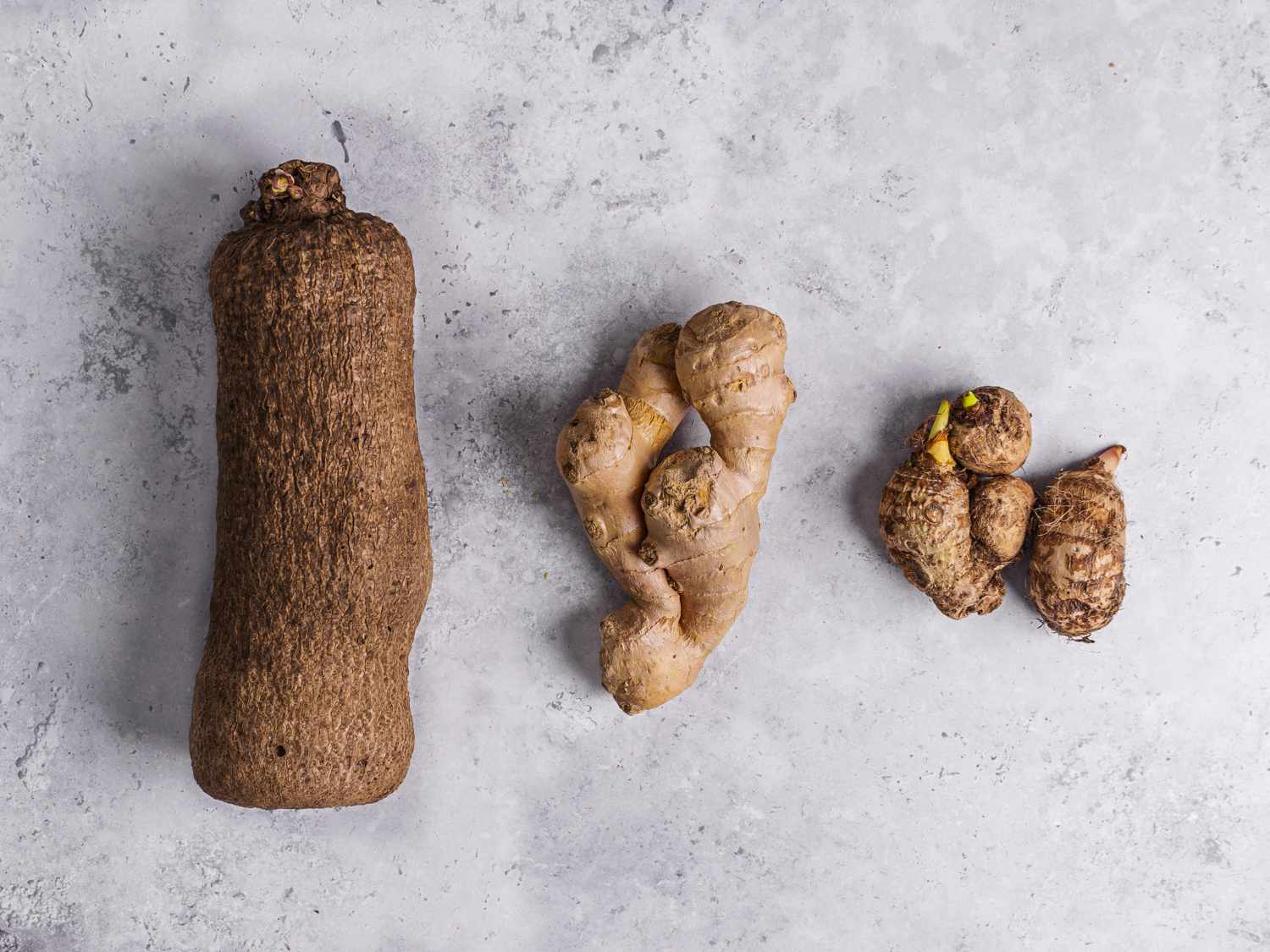 Top down view of a yams, cocoyam, ginger arranged in a straight line on a marbled grey background