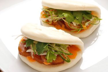 Closeup of two Steamed Buns With Simmered Daikon and Shiitake, Pickled Bean Sprouts, and Spicy Mayonnaise, served on a white plate.