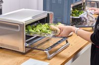 A person places broccoli into the Breville The Smart Oven Air Fryer Compact