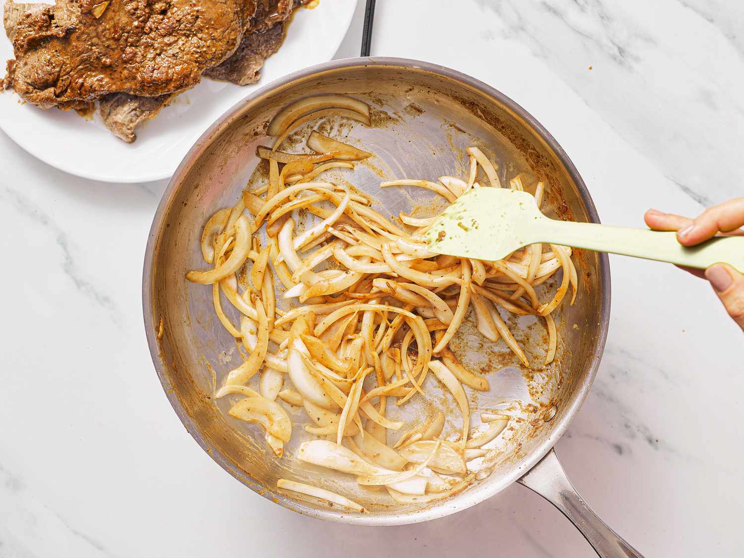 Cooking onions in a pan with steak on a plate nearby