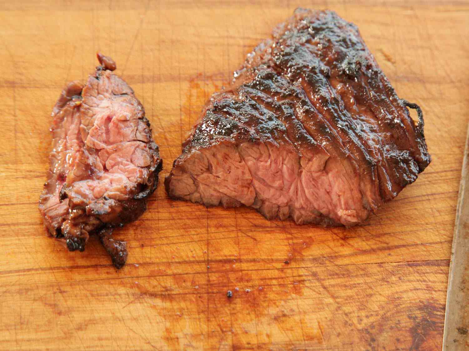 Marinated and cooked skirt steak for fajitas, next to a single slice of steak, on a wooden cutting board.