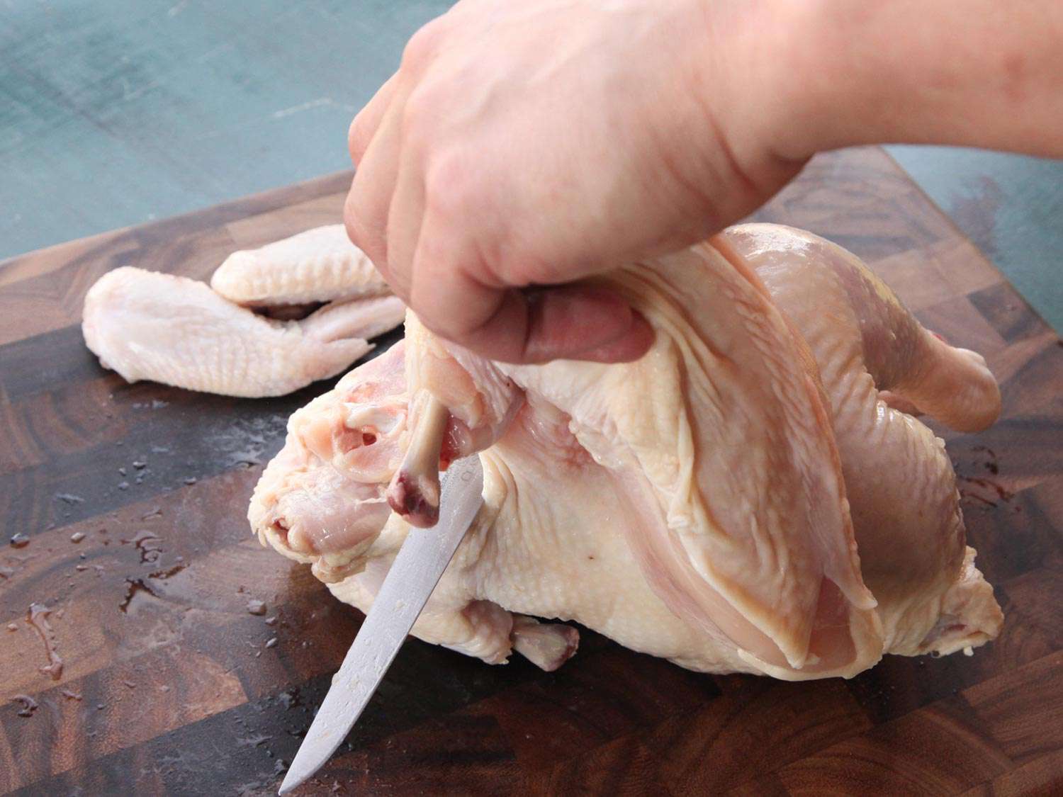 A hand holding part of a chicken as a boning knife slices into it.