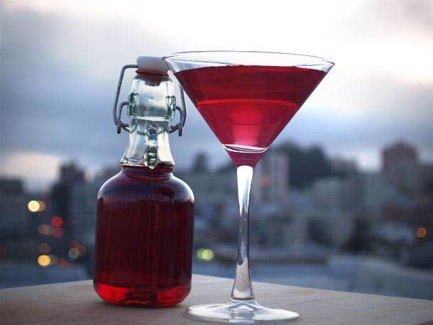 A bottle of DIY grenadine sits next to a large martini glass filled with a grenadine-tinged cocktail.