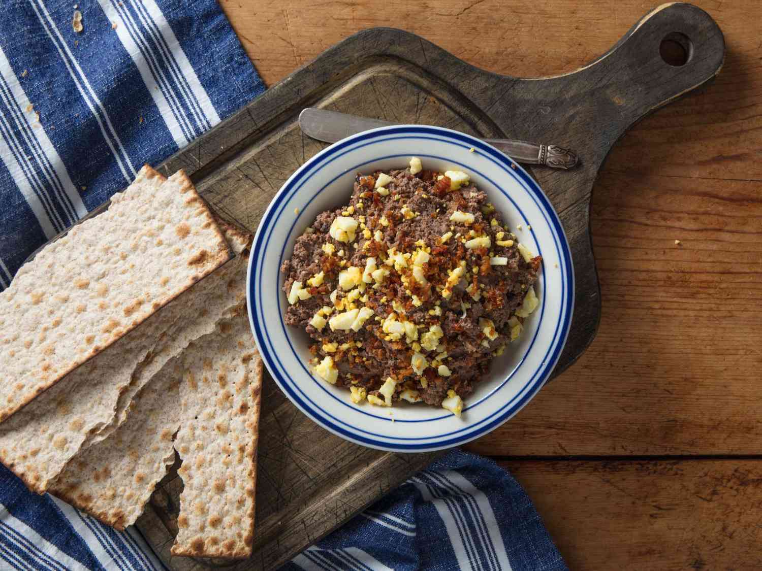 A bowl of chopped liver with matzo crackers on a wooden board.