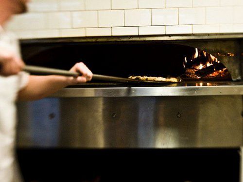 Man putting a pizza into a wood-fired oven at Pizzology in Indianapolis.