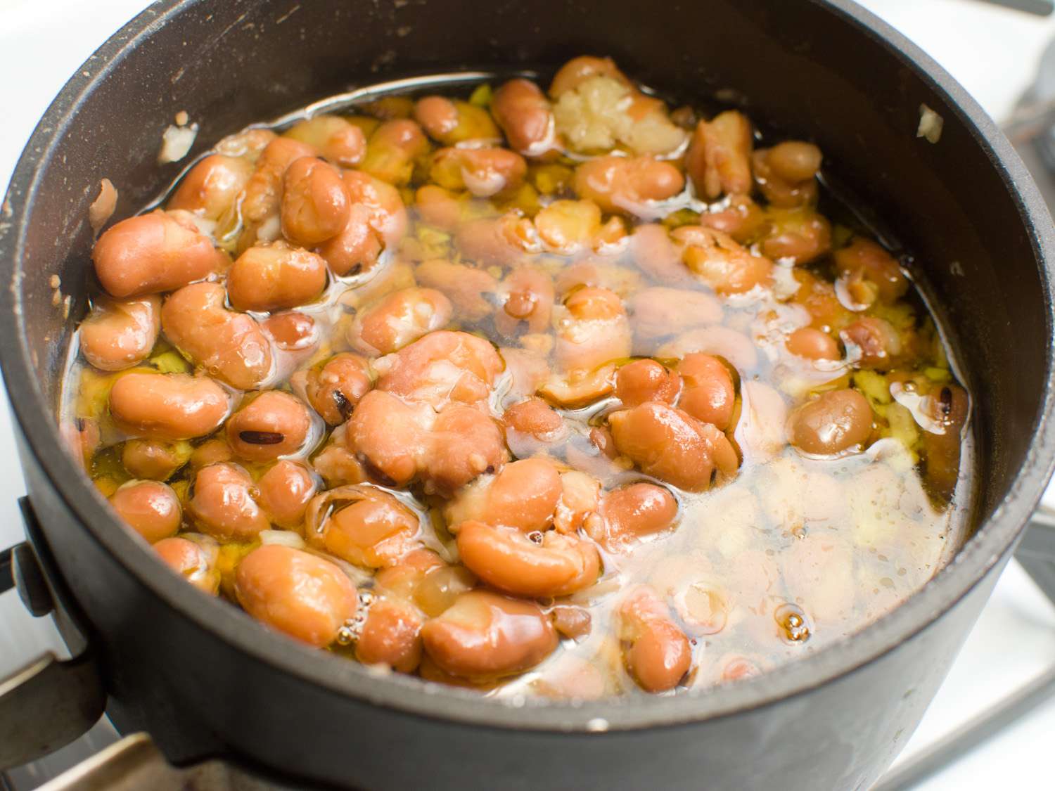 A saucepan of fava beans partially submerged in broth and a healthy quantity of olive oil, ready to simmer.