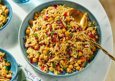 A bowl of orzo pasta salad with chickpeas, garnished with fresh herbs, served with utensils