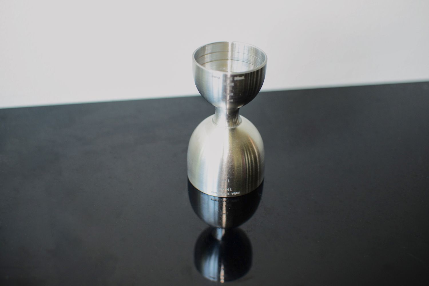 A bell-style dual-sided jigger on a black countertop