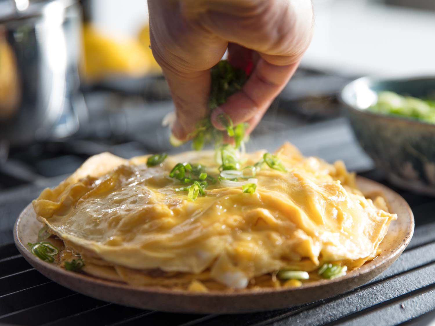 Scallions being scattered over Chinese-style layered omelette.