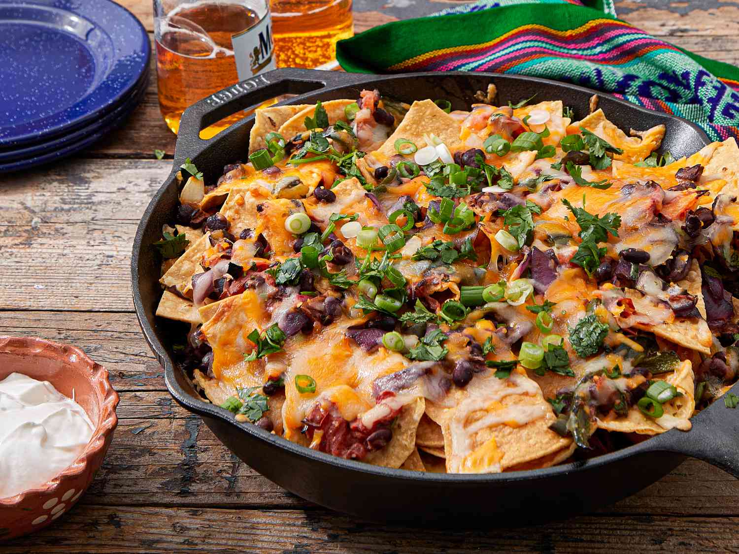 Plate of loaded nachos with melted cheese and garnishes, served in a skillet on a table
