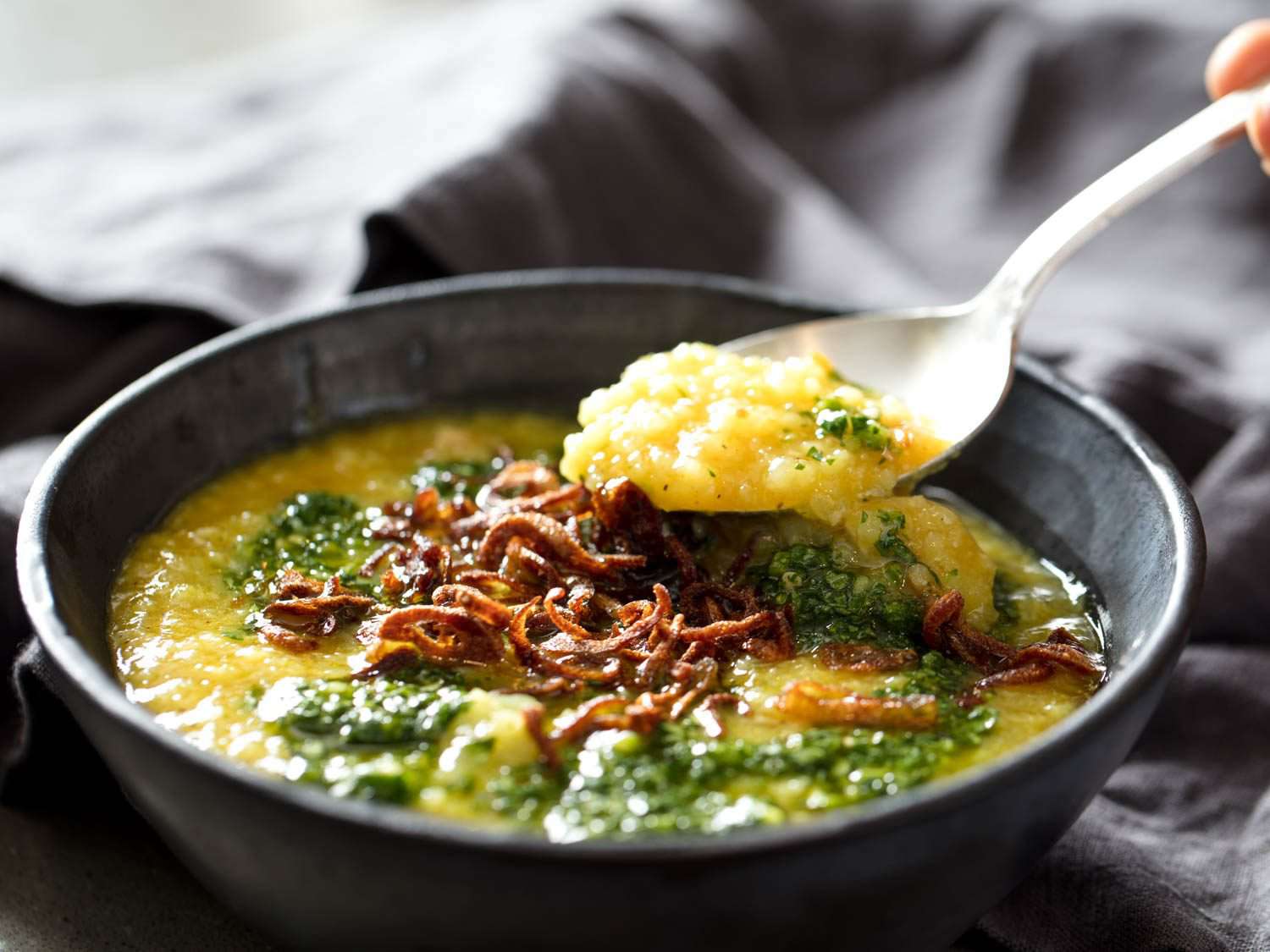 The finished Bengali porridge is served in a dark ceramic bowl. A spoon lifts up a bite of the golden porridge to the camera.