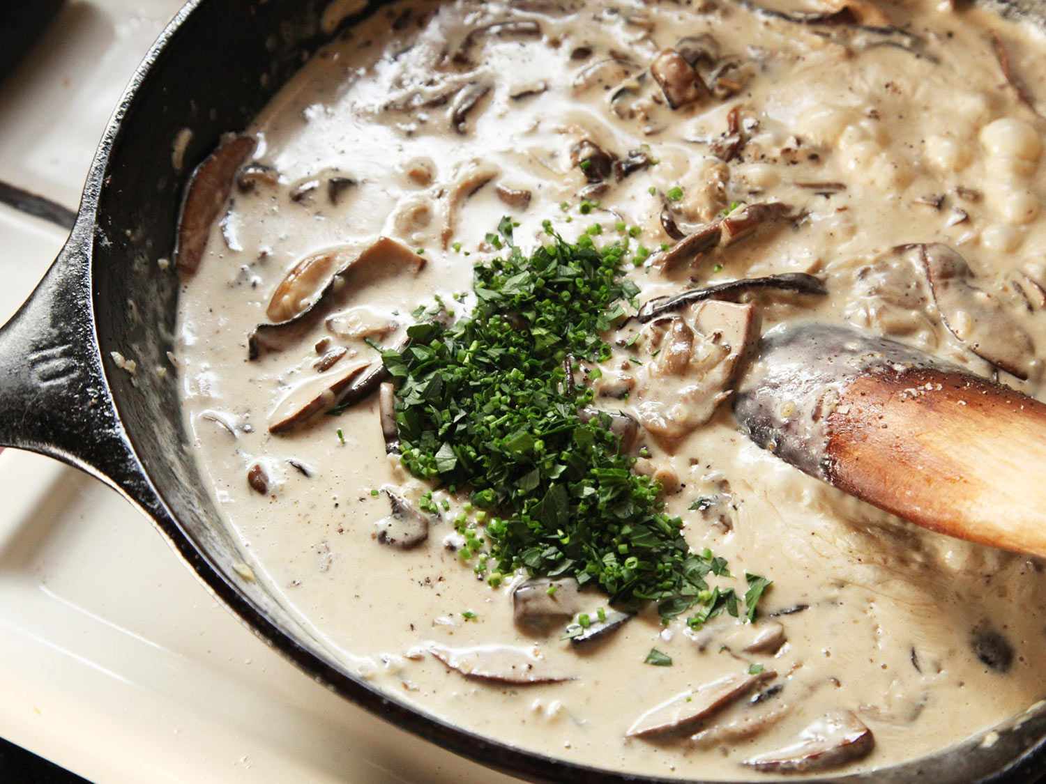 Stirring fresh parsley and chives into the sauce.