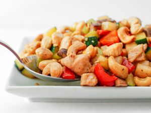 A dish of cashew chicken ding on a white plate with a serving spoon.