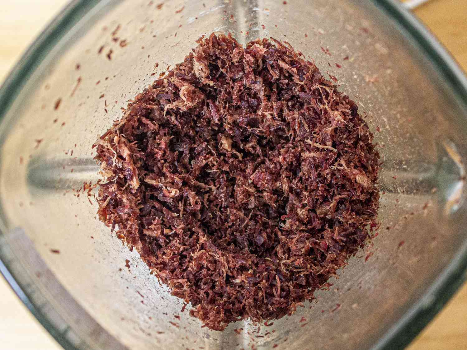 Overhead view into a blender showing broken down beef jerky after being blended