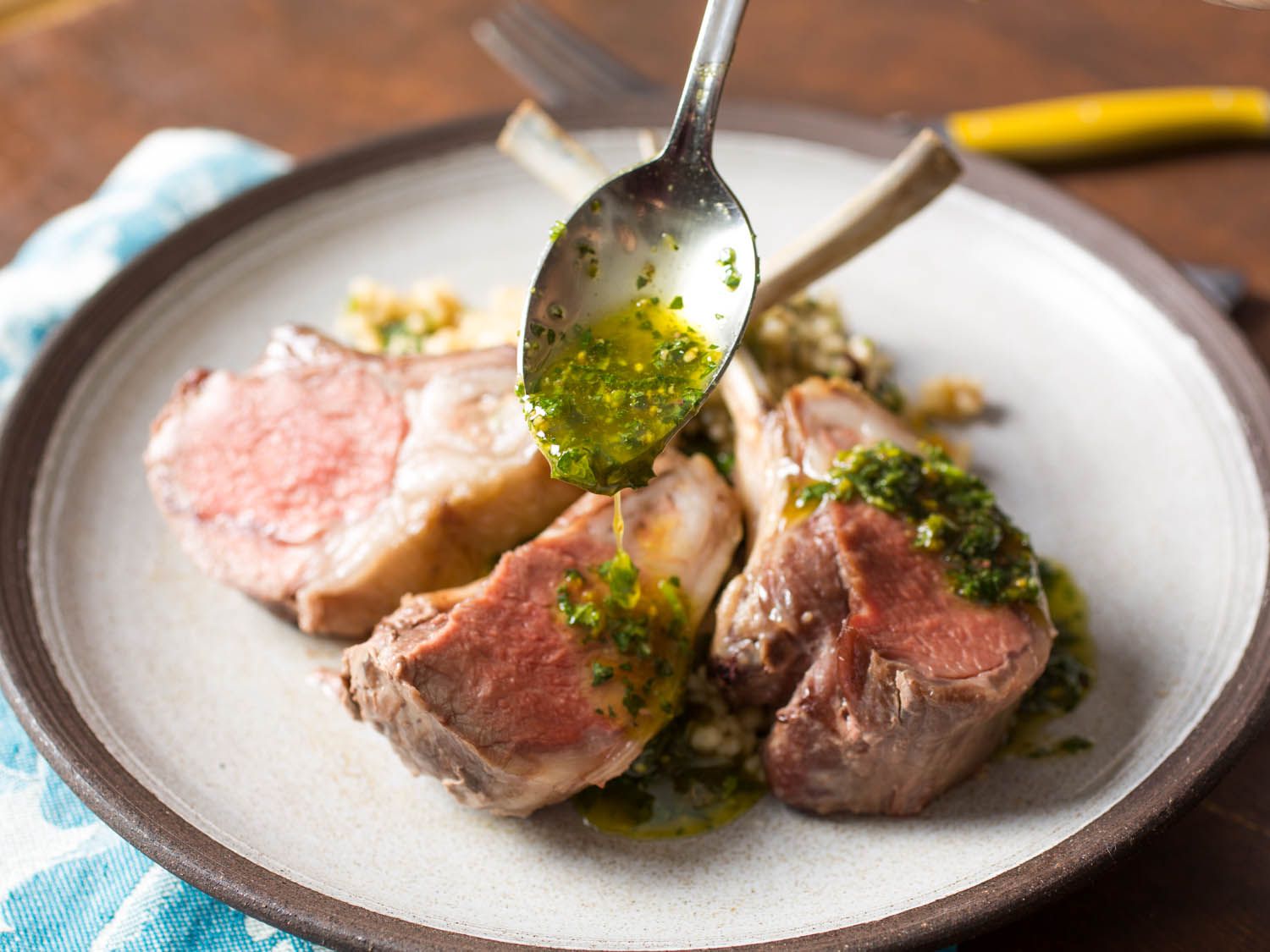 A spoon drizzling pistachio-mint sauce over lamb chops on a plate.
