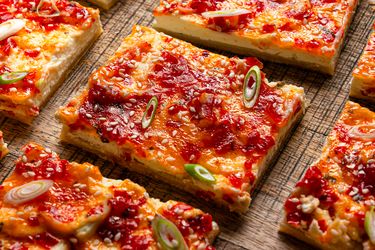 Cheese and pepper jelly tart slices garnished with sesame seeds and green onion pieces on a wooden surface