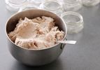 A small metal mixing bowl filled with pork rillettes. Wide-mouth quarter-pint jars are arrayed in the background.