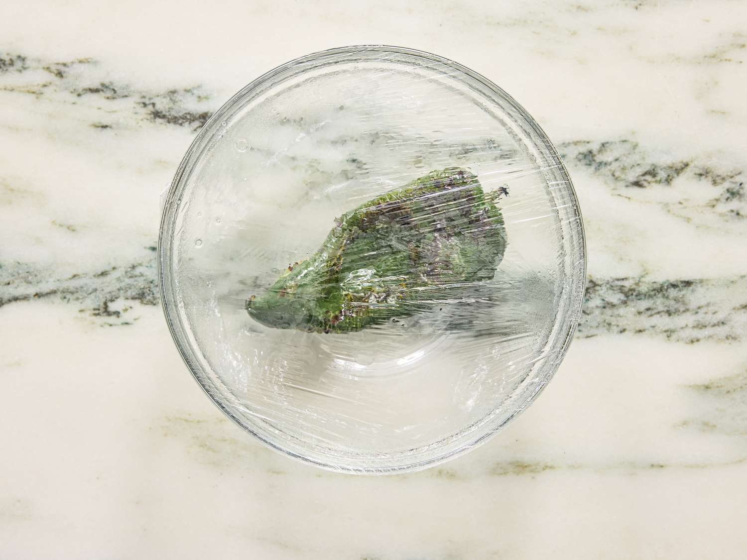A bowl with wrapped greens inside on a marble countertop