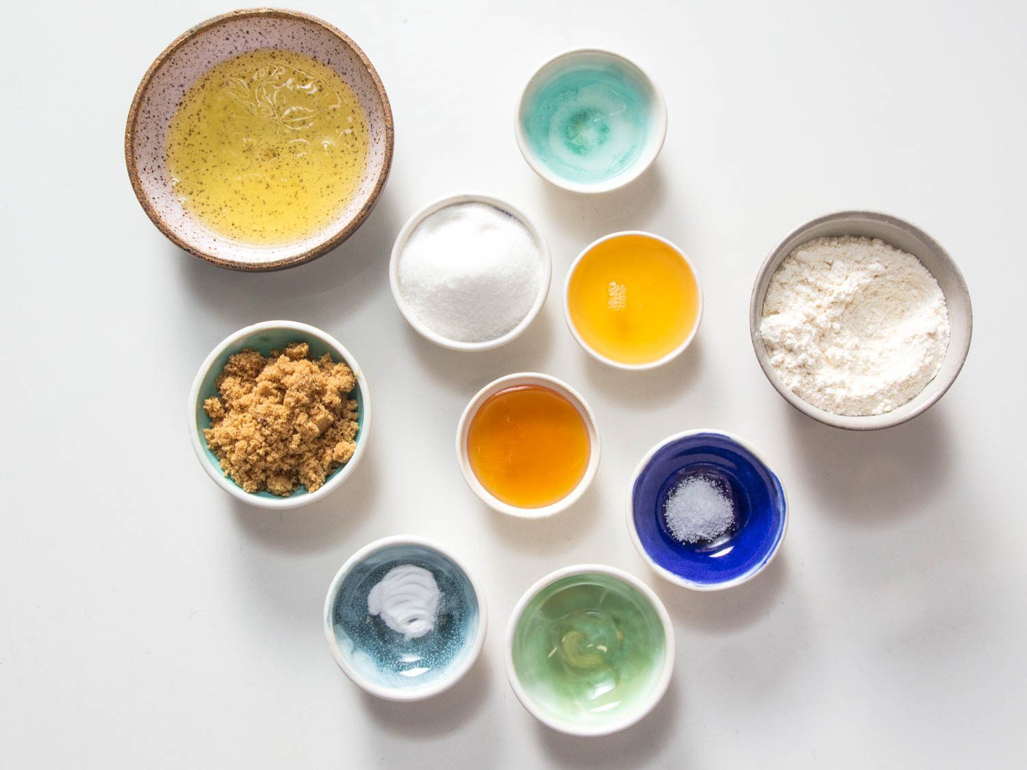 Waffle cone ingredients on a white countertop: egg whites, sugar, honey, hazelnut oil, water, salt, baking soda, and bread flour. 