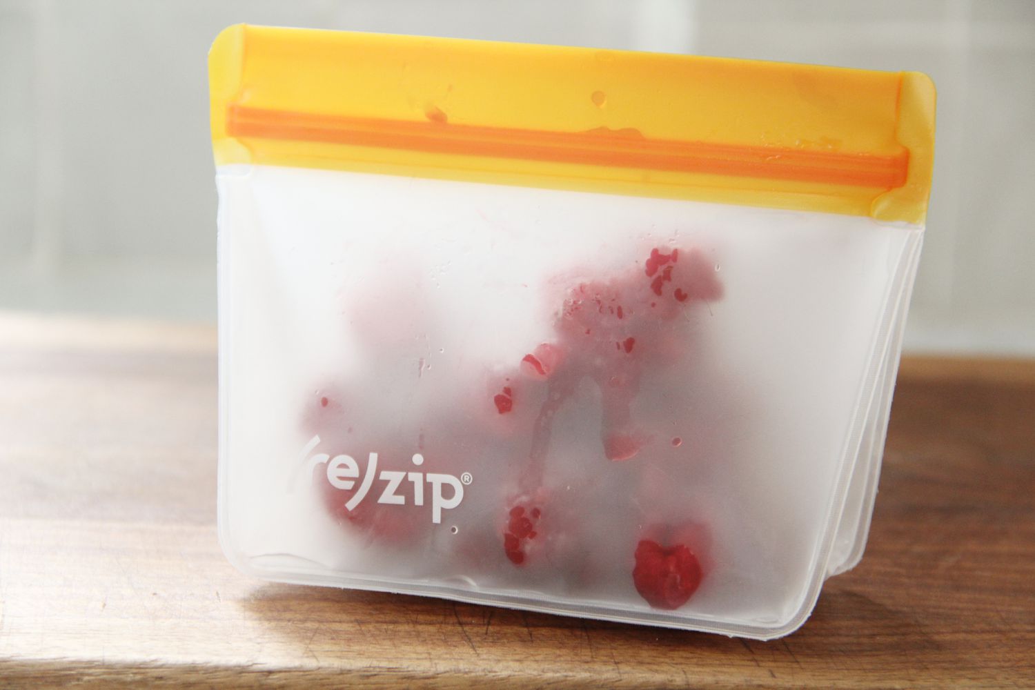 Reusable zip-top bag containing raspberries displayed on a wooden surface