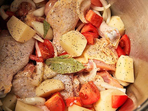 Seasoning chicken, potatoes, tomatoes, and onions in a mixing bowl.