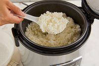 A spatula lifting up rice up out of a rice cooker.