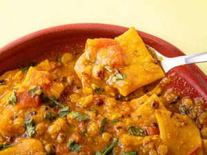 A spoonful of lentil curry with vegetables and garnished herbs being lifted from a bowl
