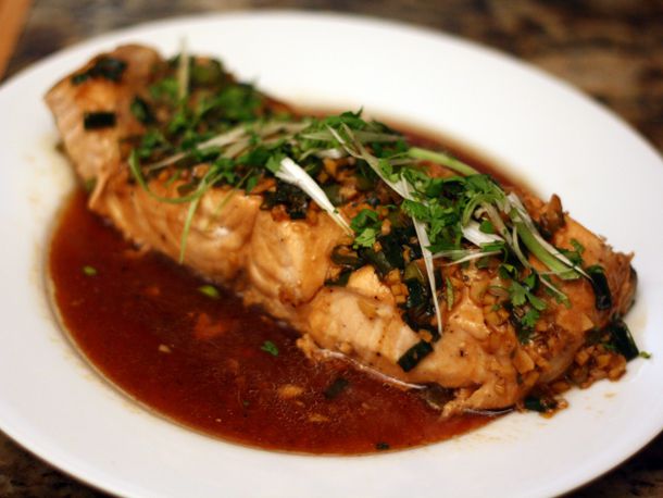 A steamed salmon fillet garnished with scallions and sitting in a flavorful sauce.