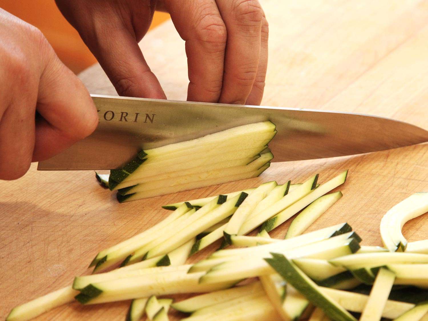 Closeup of author cutting stacks of thin zucchini slices into thin matchsticks.