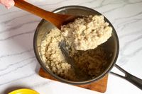 A FAAY Teak Cooking Spoon holding oatmeal above a pot of cooked oats