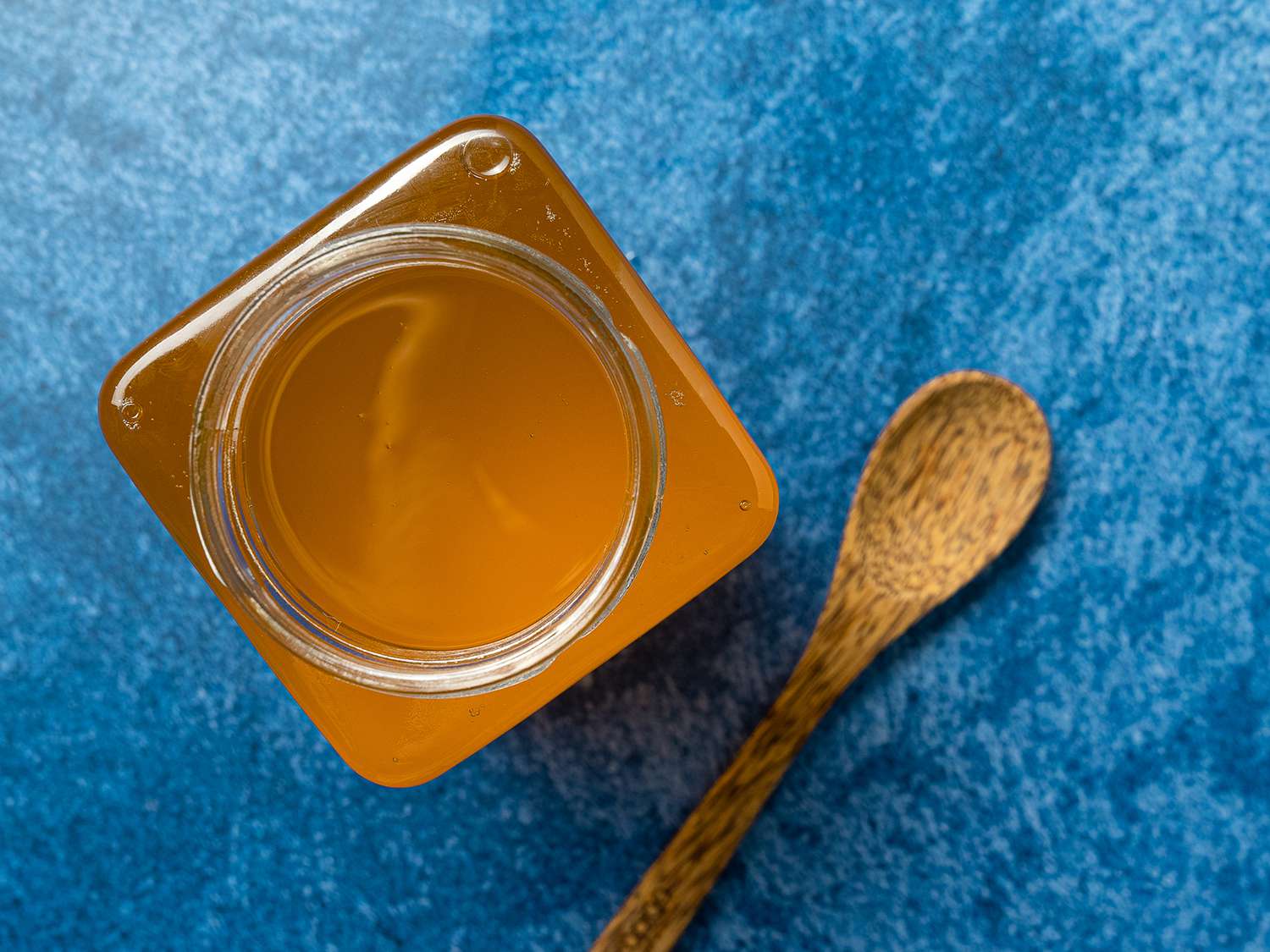 Overhead closeup of Clarified Butter in a square jar, set on a blue background.