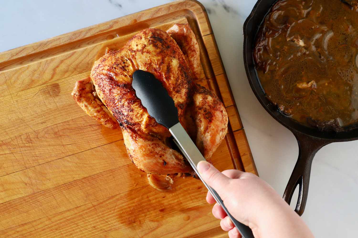 A person using the Gorilla Grip Stainless Steel Kitchen Tongs to pick up a whole chicken