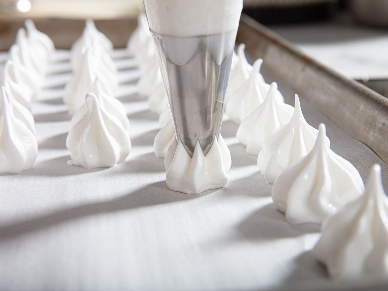 Piping meringues onto a baking sheet.