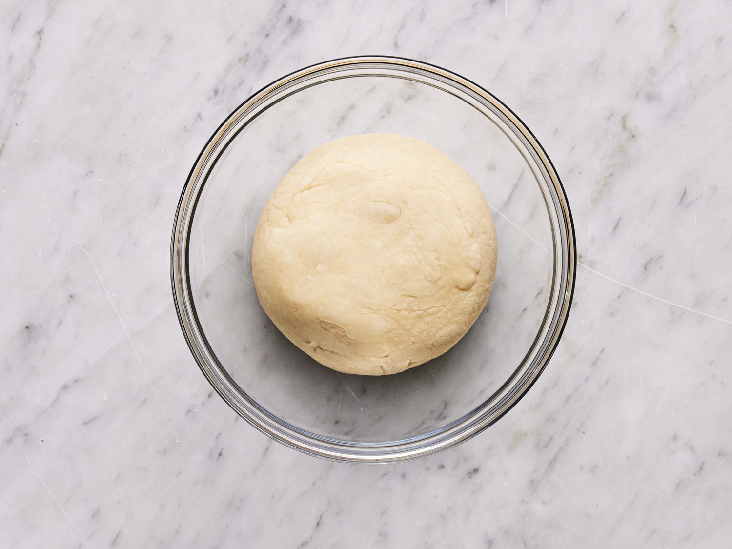 Overhead view of dough shaped into a bowl resting in a glass bowl