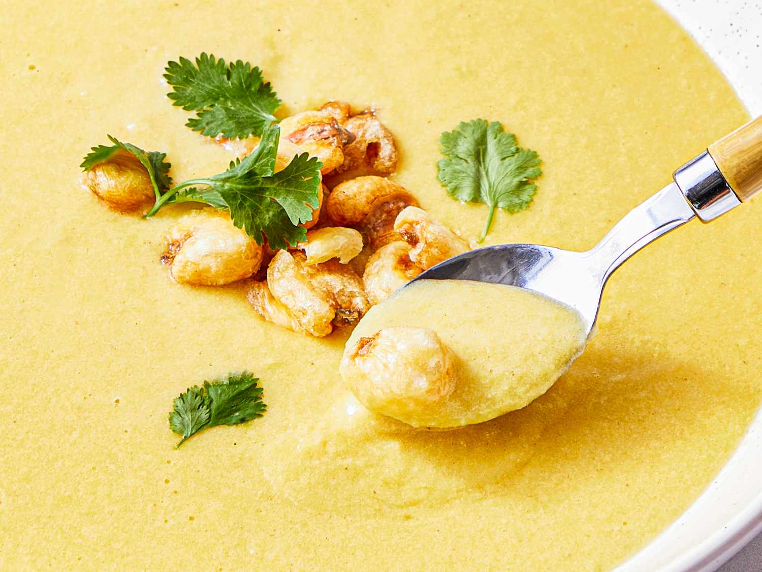 A spoonful of creamy corn soup with garnishes including herbs and toasted corn