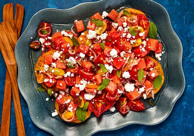 A dark bowl with tomato-watermelon salad, sprinkled with mint and feta, 