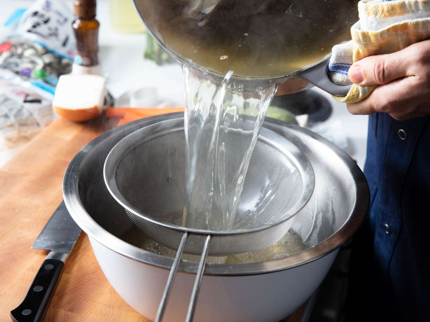 Straining out solids from broth by pouring into a fine-meshed sieve over a larger bowl.