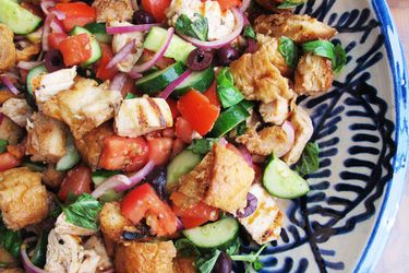 A close up of panzanella salad with grilled chicken, grilled bread, and lots of vegetables.