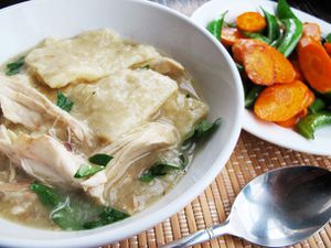 A soup bowl with a helping of chicken and slick dumplings. Sautéed carrot slices and snap peas are piled on a plate nearby.
