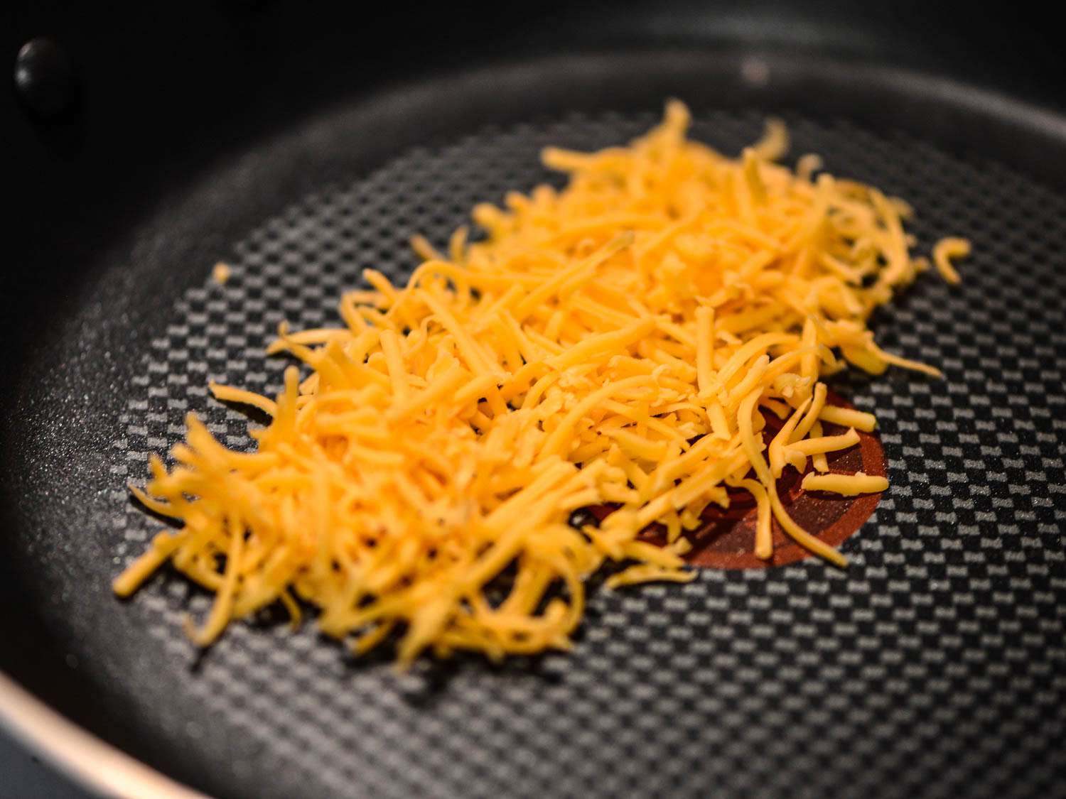 Cheddar cheese melting in a nonstick skillet.