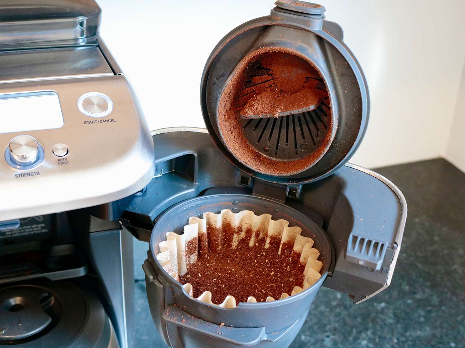 An open filter basket on a coffee maker shows ground coffee in a filter