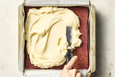 spreading frosting on top of square pan of red velvet brownies 