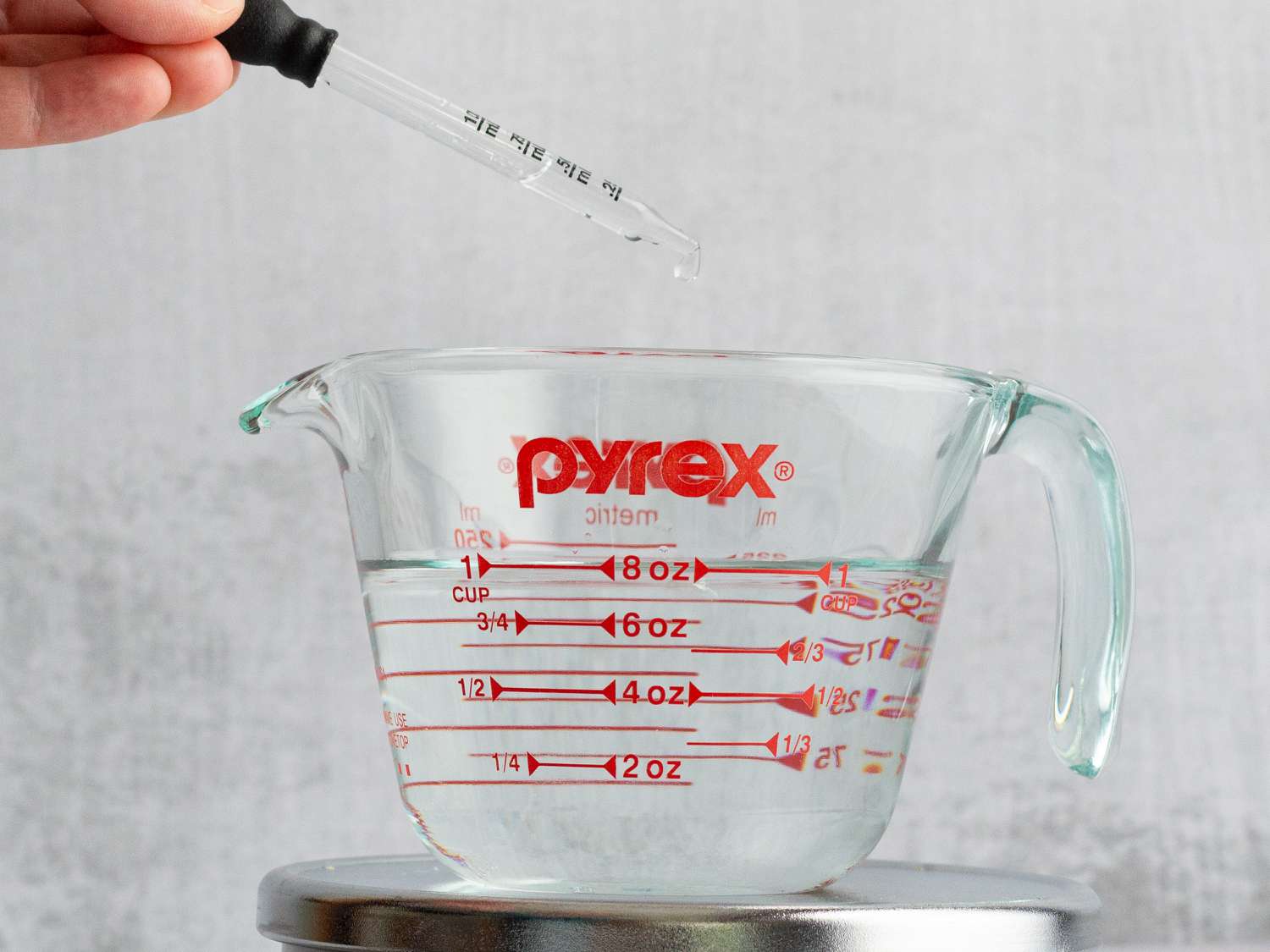 A person using an eyedropper to add water to a liquid measuring cup.