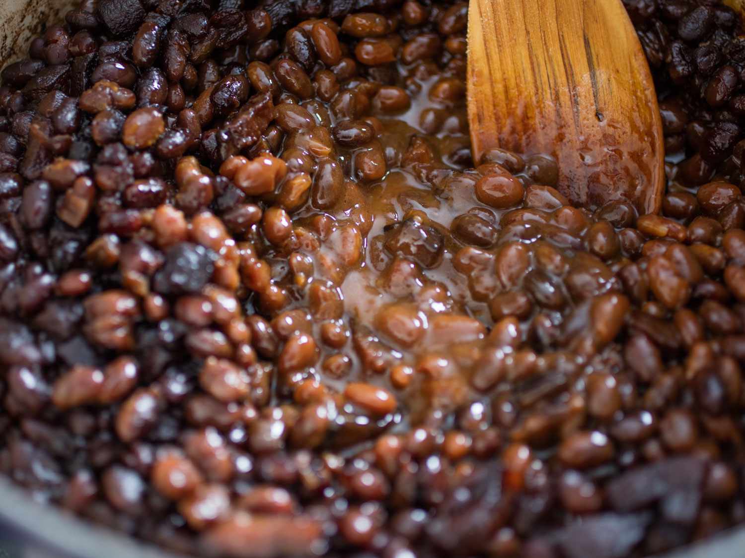 Stirring finished pot Boston baked beans with a wooden spoon.