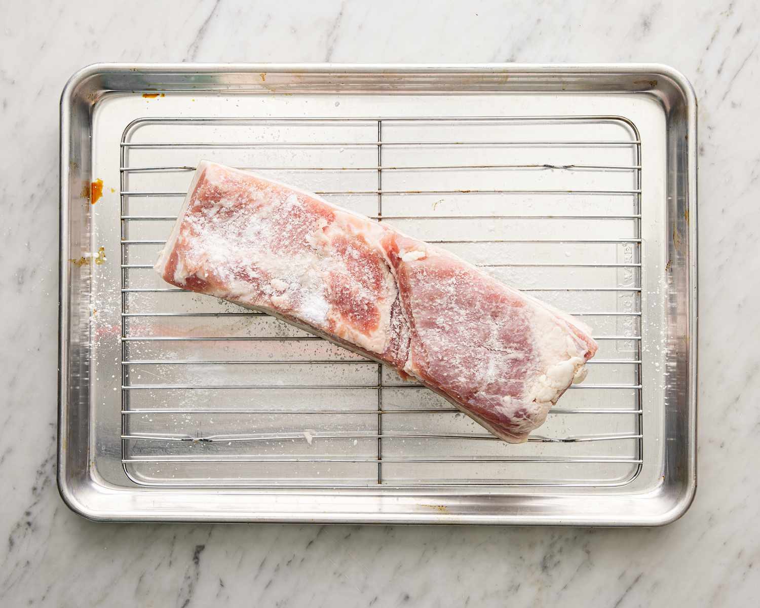 Raw pork belly over a wire rack rubbed with baking soda and salt.